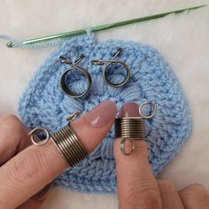 a woman is holding two rings in front of a crocheted blue bag with yarn