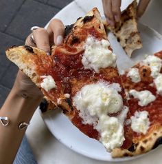 two slices of pizza on a plate being held by someone's hands over the edge