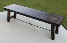 a wooden bench sitting on top of a cement floor in front of green grass and trees