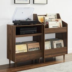 a record player sitting on top of a wooden book shelf next to a wall with two pictures above it