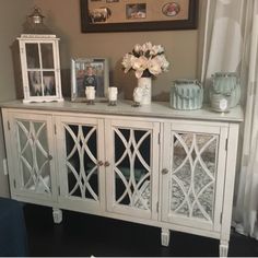 a white sideboard with glass doors and vases on top of it in front of a window