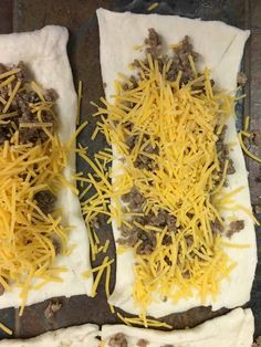 two uncooked pizzas covered in cheese and ground beef on a baking sheet