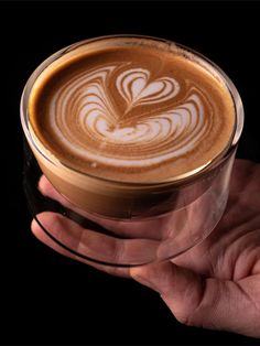 a person holding a cup of coffee in their hand, with the foam on it