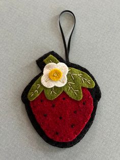 a felt strawberry ornament with a flower on it's side hanging from a black cord