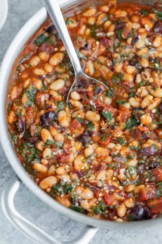 a large pot filled with beans and other vegetables on top of a table next to a spoon