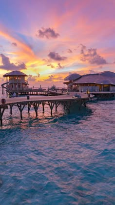 a pier with umbrellas in the water at sunset