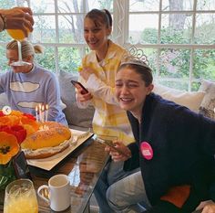 three people sitting around a table with food and drinks on it, one person holding a cell phone