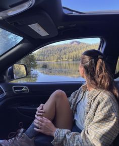 a woman sitting in the passenger seat of a car next to a lake and mountains