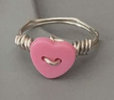 a pink heart shaped button is attached to a silver wire ring on a gray surface