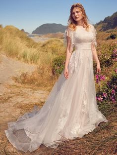 a woman in a white wedding dress standing on the side of a hill next to flowers