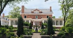 a large red brick house surrounded by trees and shrubs with a walkway leading to the front door