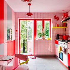 a kitchen with red and pink walls, white tile flooring and an open door leading to the outside