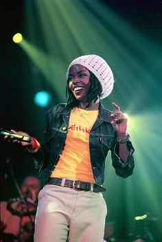 a woman standing on top of a stage wearing a hat and holding a cell phone