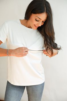 a woman is cutting her hair with scissors and looking at the camera while wearing a white t - shirt