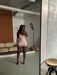 a woman in a pink dress is taking a selfie with her cell phone while standing next to a chair