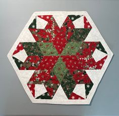 a red and green patchwork quilt on a wall hanging from the side of a gray wall