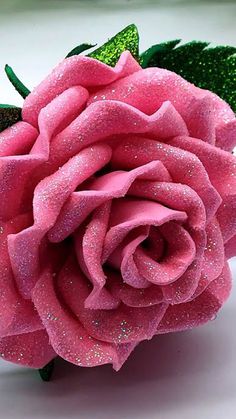 a pink rose with glitters on it sitting on a white counter top next to a green leaf