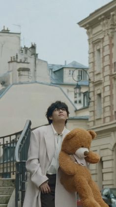 a man standing next to a teddy bear on the steps in front of a building