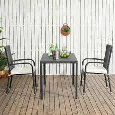 two chairs and a table on a wooden floor with white walls behind them, in front of a potted plant