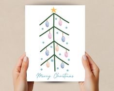 two hands holding up a card with a christmas tree on it