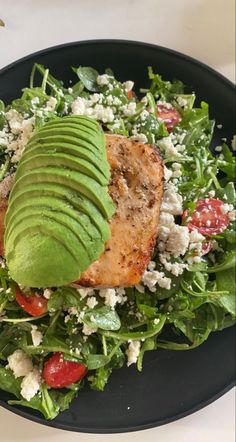 a salad with salmon, avocado and tomatoes is on a black platter