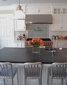 a kitchen with white cabinets and black counter tops, flowers in a vase on the island