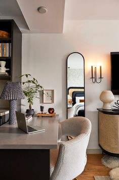 a room with a desk, chair, mirror and laptop on the table in front of it