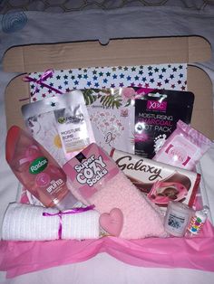 an open box filled with lots of items on top of a white bed covered in pink ribbon