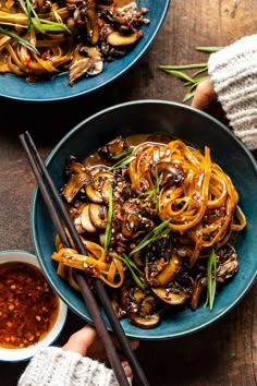 two bowls filled with noodles and mushrooms next to chopsticks