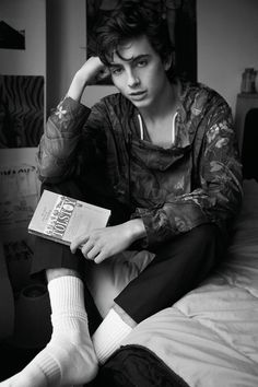 a young man sitting on top of a bed next to a book in his hand