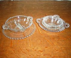 two glass dishes sitting on top of a wooden table with beaded trim around the edges