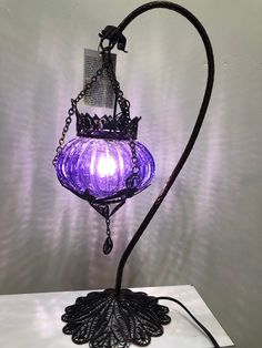 a purple light is hanging from a black metal holder on a white surface with a chain attached to it