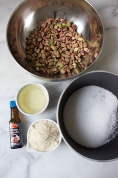 ingredients to make pistachio cake displayed in bowls on marble counter top, including flour, sugar and oil