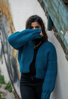 a woman leaning against a wall with her hand on her face and wearing a blue sweater