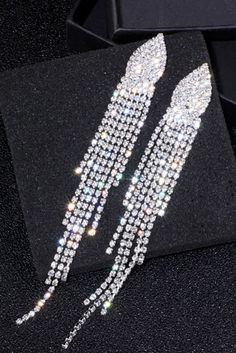 two pairs of long crystal earrings on a black box with some other items in the background