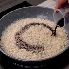 someone is adding brown rice to a skillet