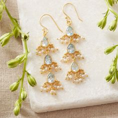 These stunningly bright pale Blue Topaz and Beaded Seed Pearl 18K Gold plated drop earrings are exquisitely crafted. The 3 teardrop shaped Blue Topaz gemstones are beautifully set in 18K gold over Sterling Silver and seed pearl beads surround each  gemstone. There are 3 stones in each earring as well as 2 seed pearl beads on either side of each gemstone. The length of the earrings help to elongate the neck and also create movement while wearing.  Blue Topaz are the birthstone for those born in December, making these a perfect birthstone gift. Blue Topaz are also associated with the 4th year of marriage, making these a great anniversary gift as well.  Blue Topaz are semi-precious gemstones and have been used to symbolise many positive attributes for centuries. Blue Topaz are most often a sy Delicate Gemstone Earrings For Wedding, White Gemstone Accented Earrings For Wedding, Wedding Gemstone Drop Chandelier Earrings, Festive Wedding Jewelry With Gemstone Accents, Teardrop Gemstone Chandelier Earrings For Wedding, Drop Earrings With Gemstone Accents For Weddings, Wedding Gemstone Drop Earrings, Blue Topaz Dangle Jewelry For Wedding, Wedding Drop Gemstone Earrings