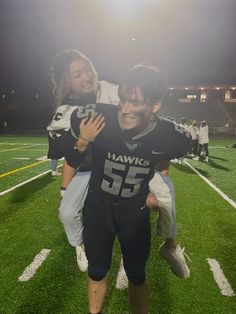 a man and woman in football uniforms standing on a field with their arms around each other