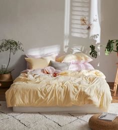 a bed with yellow sheets and pillows in a room next to a potted plant