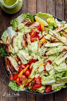 a salad with chicken, lettuce and tomatoes on it next to a cup of dressing