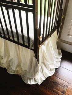 a crib with white ruffles on the bottom and wood flooring in front of it