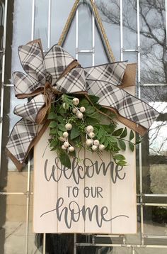 a welcome to our home sign hanging on a door with a burluck bow