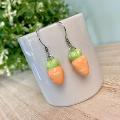 two small carrots are hanging from silver earwires on a table next to a potted plant