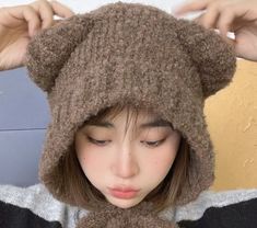 a woman wearing a brown bear ear flap hat with her eyes closed and hands behind her head