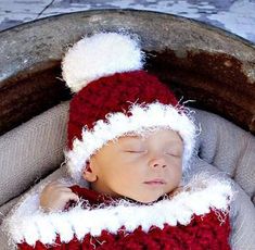 a newborn baby wearing a red and white crocheted santa hat sleeping in a bucket