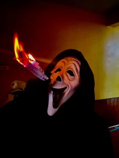 a person wearing a mask and holding a knife in front of their face with fire coming out of it