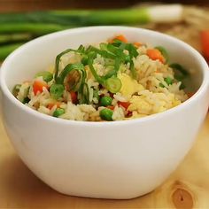 a white bowl filled with rice and vegetables on top of a wooden table next to asparagus