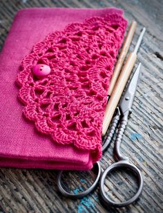 a pair of scissors and a pink crochet doily on a wooden table