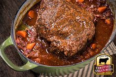 beef stew with carrots and potatoes in a green pot on a striped cloth next to a wooden table