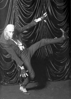 an old black and white photo of two people doing dance moves in front of a curtain